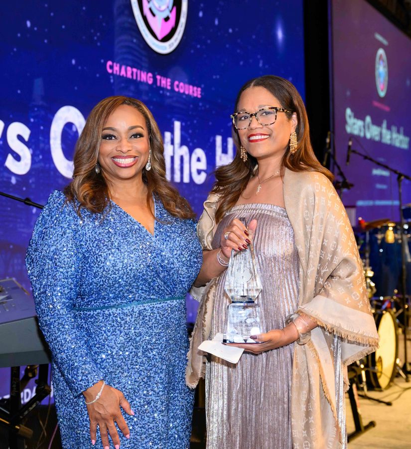 Two women on stage at the Stars Over the Harbor gala, one holding a crystal award