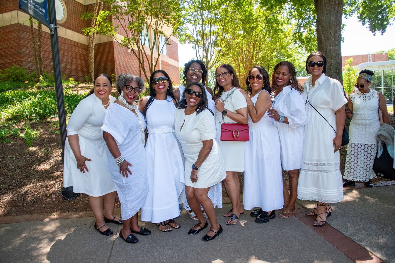 A group of women in white dresses and sunglasses gathered on a college campus